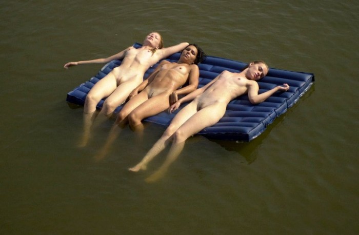 Three naked  young chicks tanning in the middle of the lake.