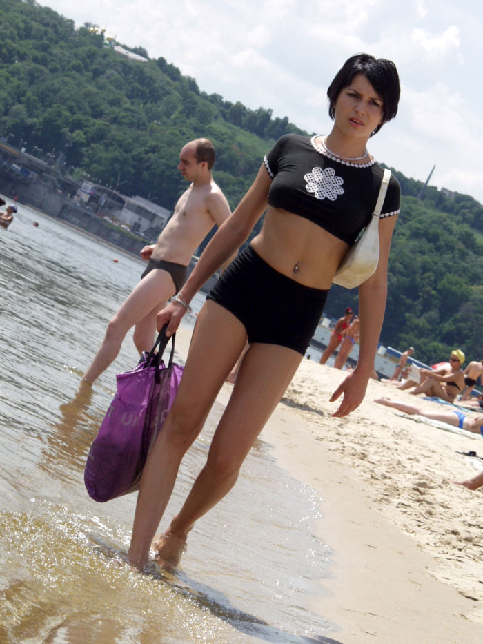 Short-haired brunette is undressing at public beach