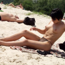 Short-haired brunette is undressing at public beach