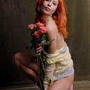 Beautiful red-haired girl with flowers is photographed naked