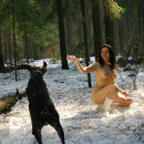 Naked girl playing snowballs with dog at winter forest
