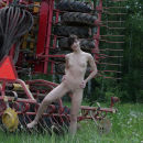 Russian girl undressing in front of a tractor on the field