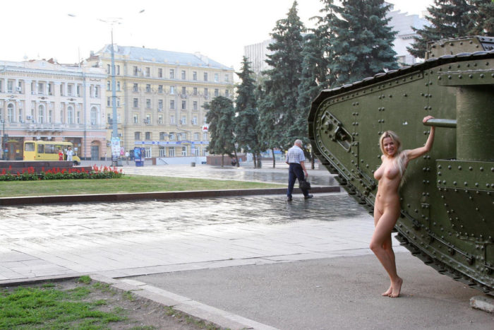 Naked girl posing next to a tank in the town square