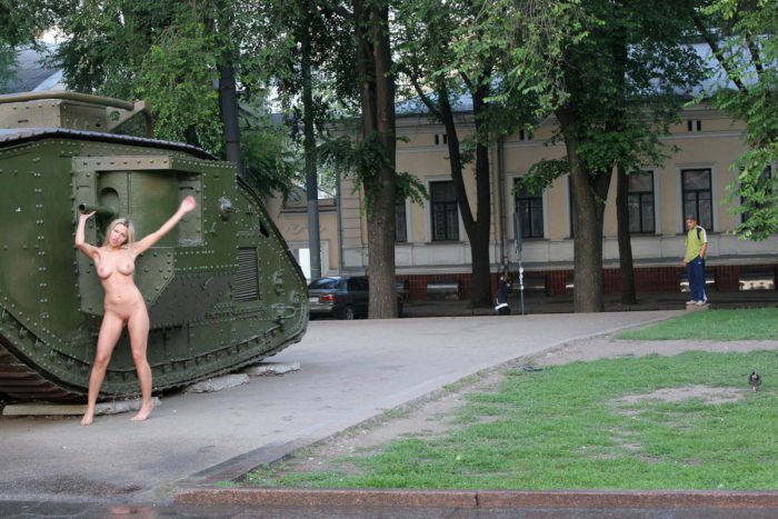 Naked girl posing next to a tank in the town square