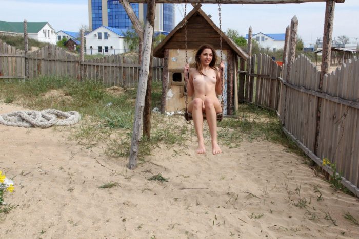 Naked girl swinging on a swing on the beach