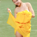 A bright yellow cloth hugs Izabel A’s naked body as she poses enthusiastically by the river.