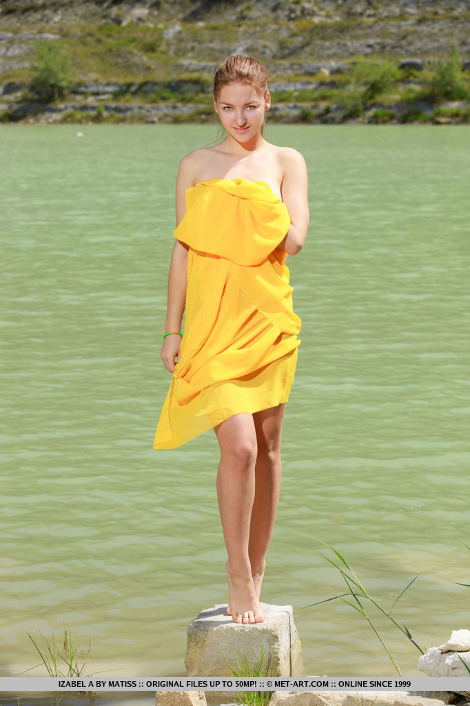 A bright yellow cloth hugs Izabel A's naked body as she poses enthusiastically by the river.