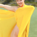 A bright yellow cloth hugs Izabel A’s naked body as she poses enthusiastically by the river.