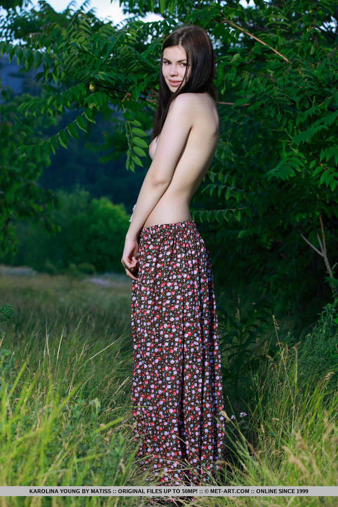 Karolina Young posing in the lush green woods. The deep verdant colors makes her smooth, pale skin stand out, and her cuppable breasts with pink nipples and shaved pussy.