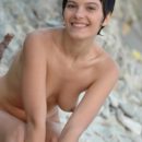 Short-haired brunette shows pussy with a smile onrocky beach