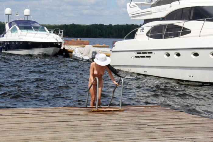 Naked brunette in white hat on the pier