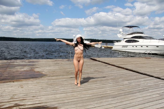 Naked brunette in white hat on the pier