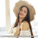 Beautiful Astrid Herrara takes off her straw hat and knitted dress by the window.