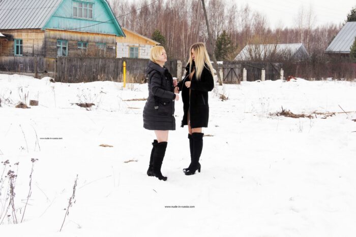 Two blondes throw snowballs at each other on a village road