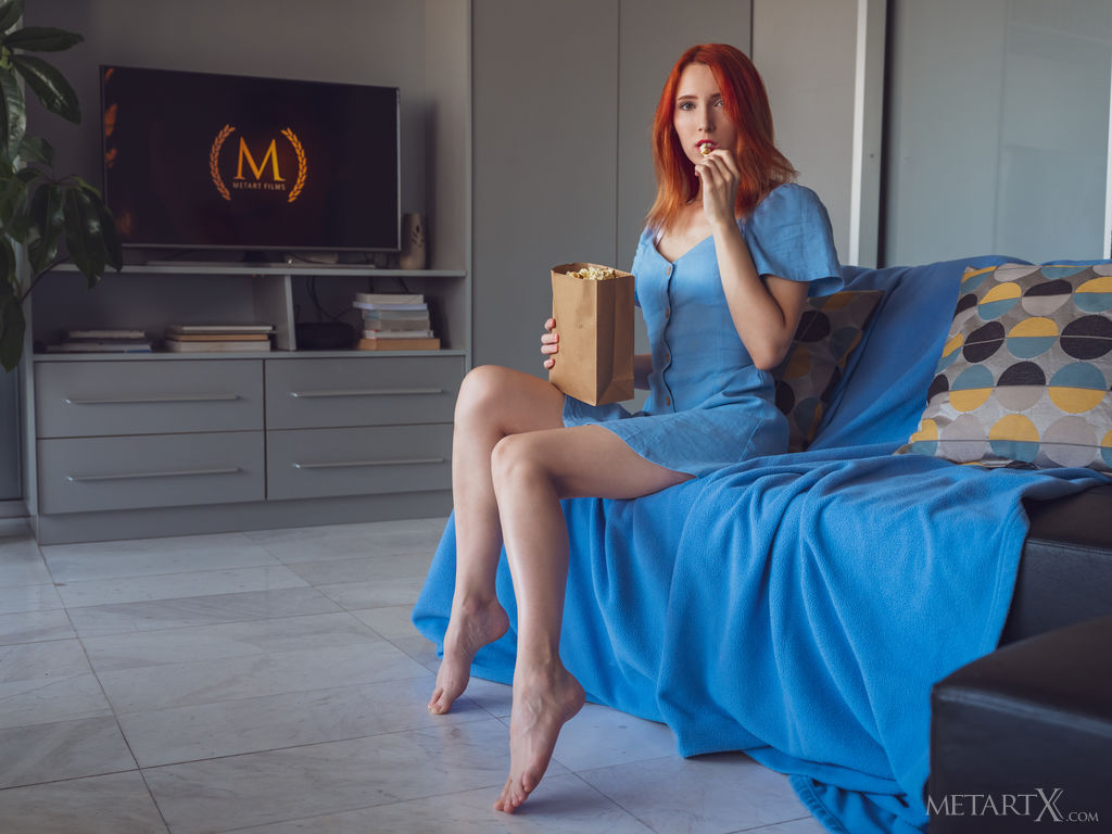Redhead Elin Flame enjoys her popcorn while watching a film in the living room. She takes off her short dress and fingers her pussy.