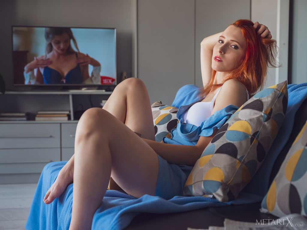 Redhead Elin Flame enjoys her popcorn while watching a film in the living room. She takes off her short dress and fingers her pussy.