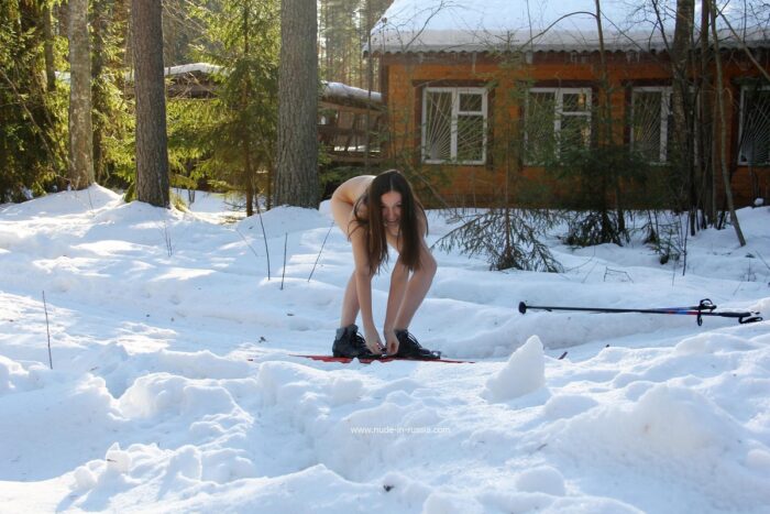 Smiling girl Lera without clothes is skiing in the forest