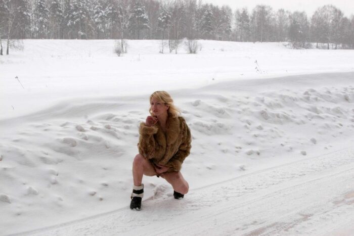 Blonde Diana takes off her fur coat on a snowy road