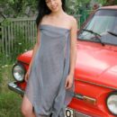 Smiling brunette Olga P with tattoo in red old car