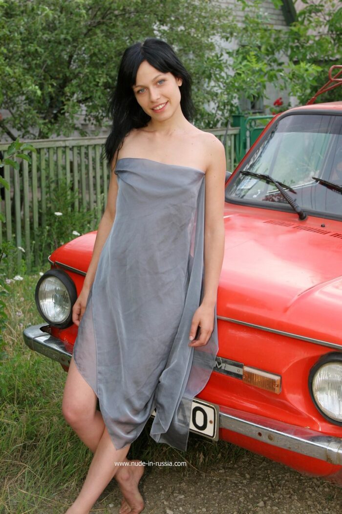 Smiling brunette Olga P with tattoo in red old car