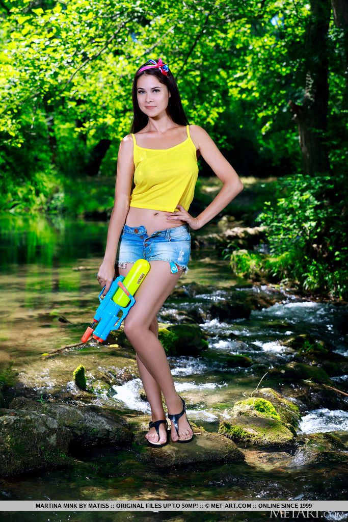 Martina Mink is ready to shoot a watergun and play by the river bank. She decides to take off her yellow tank top and shorts and uncover her juicy melons and hairless pussy.