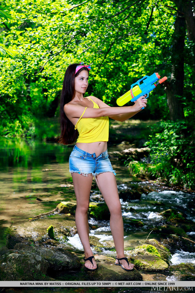 Martina Mink is ready to shoot a watergun and play by the river bank. She decides to take off her yellow tank top and shorts and uncover her juicy melons and hairless pussy.
