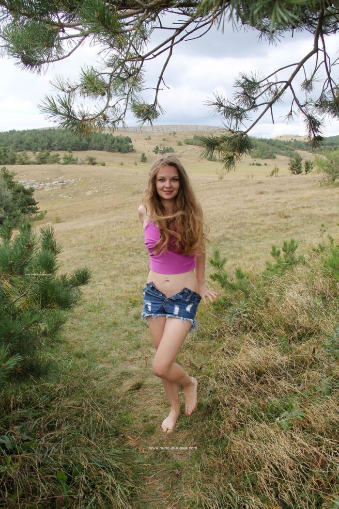Smiling blonde Anna B undresses in mountains