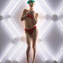 Arya teases in her red lingerie and green sun visor by the wall with lots of lights which highlights her bootylicious body and manicured landing strip.