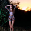 Elle Tan undresses and flashes her long sexy legs, slender body and trimmed muff in the middle of a meadow as the sun sets across the horizon