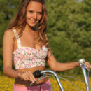 Fun, carefree and refreshingly cute, Mango exudes a pretty girl-next-door in her floral corset, skimpy pink skirt, and embellished sandals as she frolic on the grassy prairie with her bicycle.