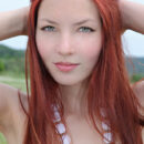 Gorgeous redhead with hypnotizing brown eyes, Nalli A’s beauty stands out in a field of flowers.