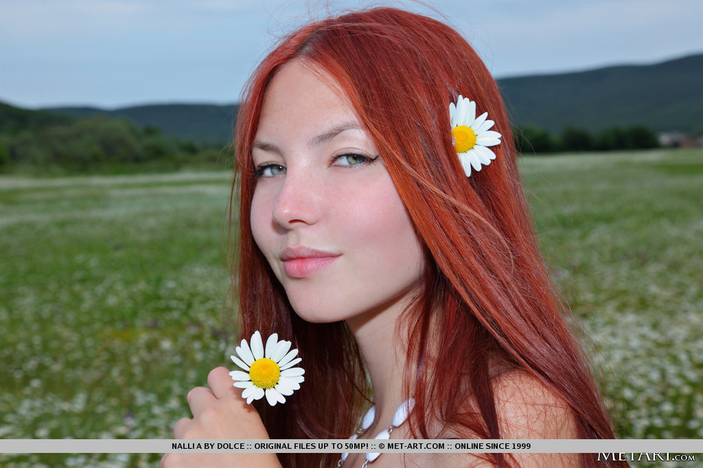 Gorgeous redhead with hypnotizing brown eyes, Nalli A's beauty stands out in a field of flowers.