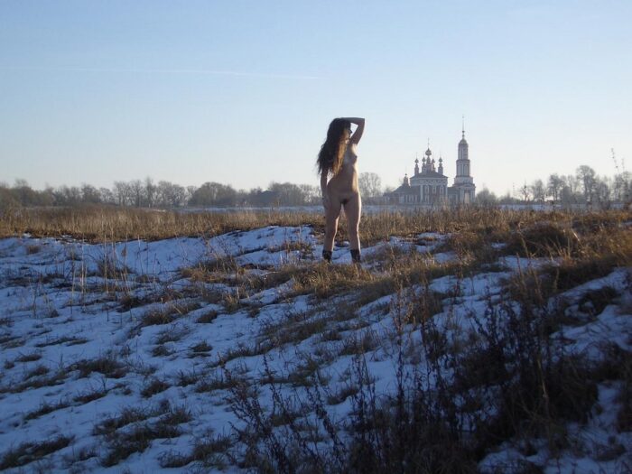 Long-haired girl Angelika without clothes posing on a snowy field
