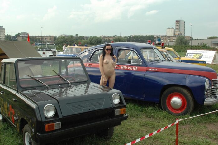 Naked brunette in sunglasses at the exhibition of old cars