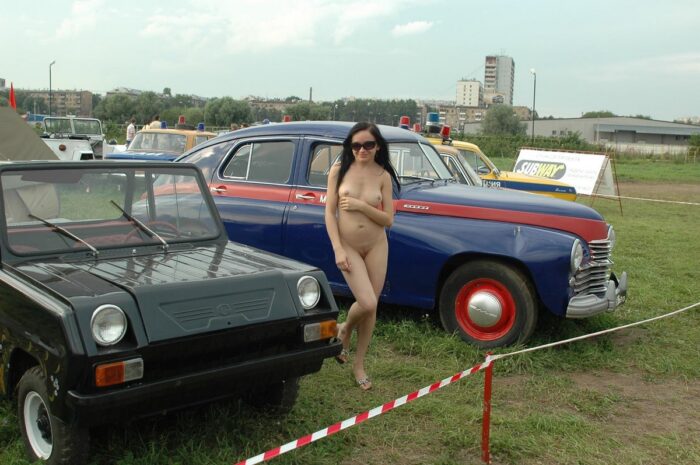 Naked brunette in sunglasses at the exhibition of old cars