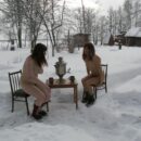 Two girls without clothes drink tea outdoors at winter