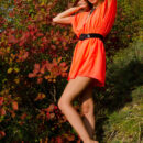 A smiling and confident Sofy frolics among the grass and plants in her bright orange dress like a carefree forest nymph.