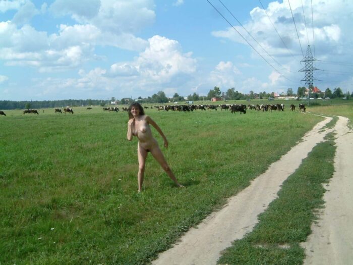 Girl Juna posing without clothes near the herd of cows