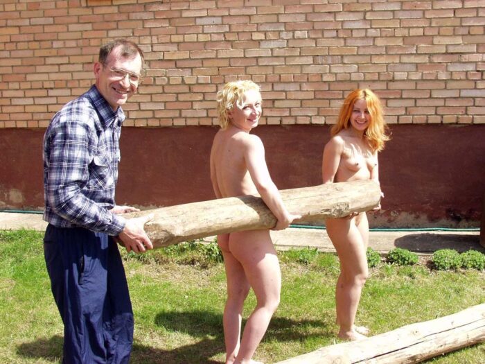 Two girls help a man saw a log naked