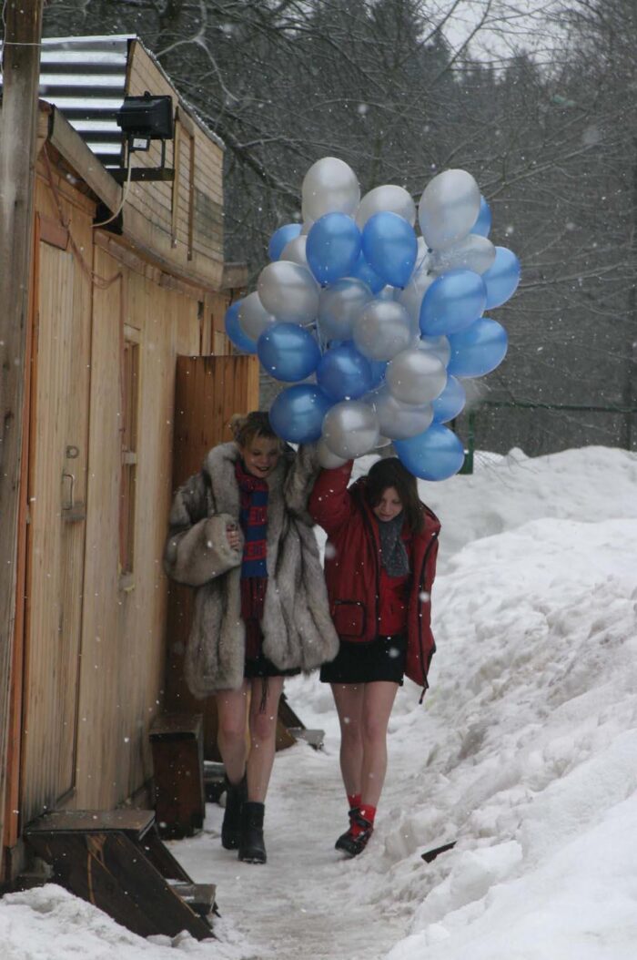 Two naked girls play with balloons at winter outdoors