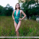 Mirabella hikes across the field in her green one-piece swimsuit. She strips it off and exposes her small tits and shaved pussy.