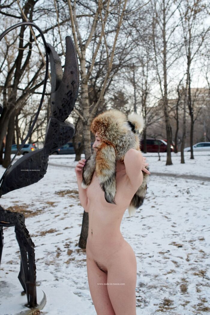 Young blonde Alexandra B posing in a fur hat in a city park