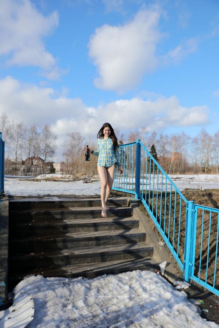 A young girl Katja P plays with a bottle of champagne on a snow-covered pier