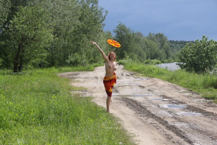 Redheaded teen Lera S plays frisbee by the river