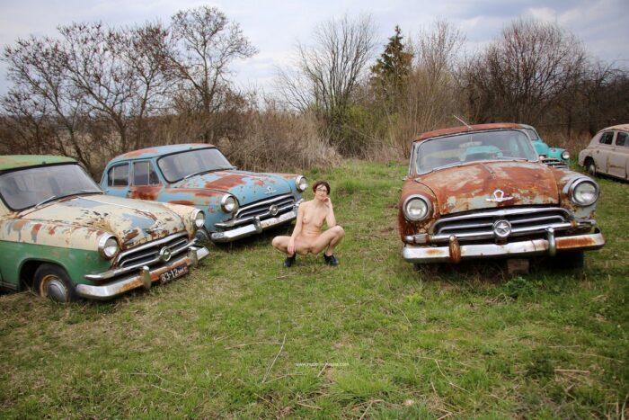 Naked russian girl in glasses poses at old car