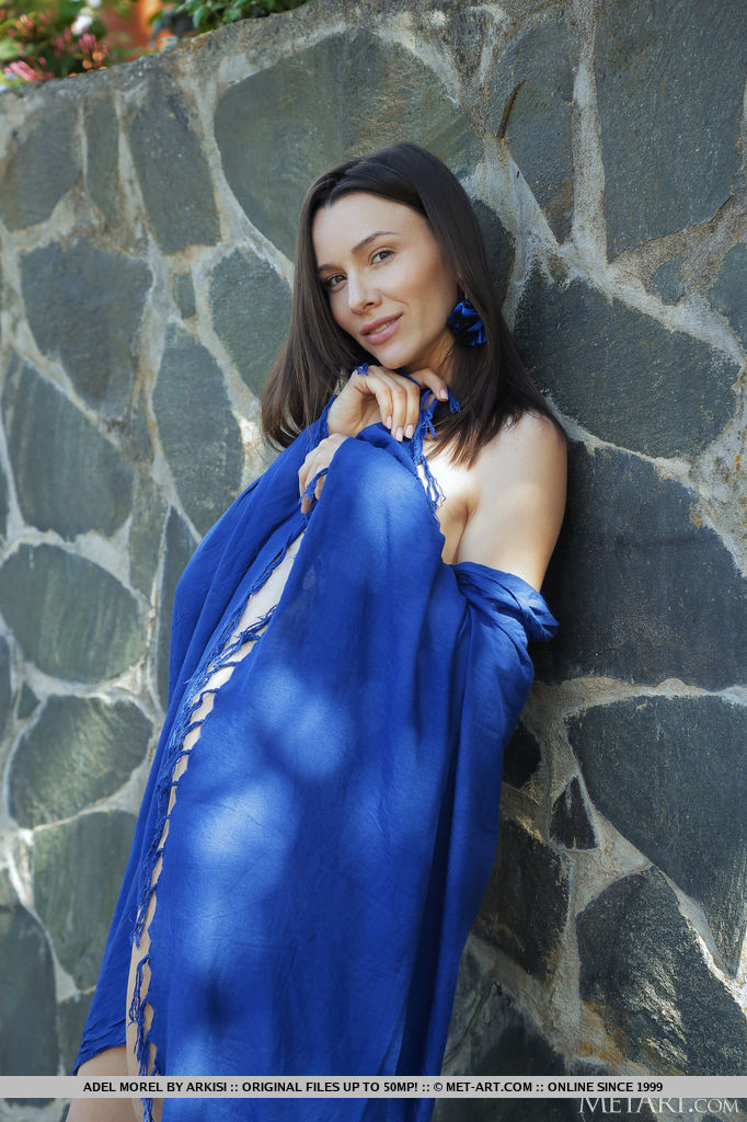 Adel Morel poses with her blue shawl by the stone wall. She lets it slip down her slender body and expose her long legs in high heels and smooth cunt.