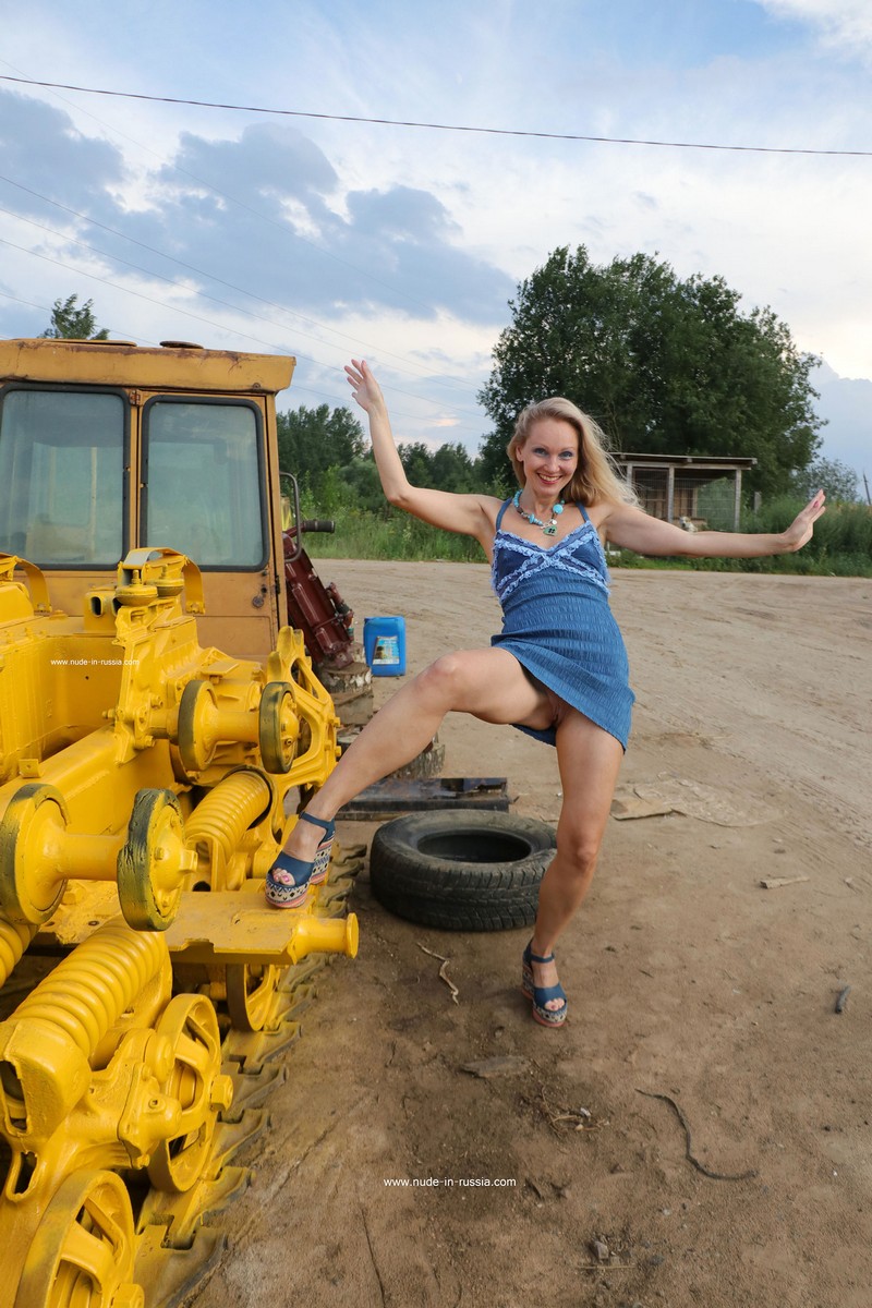 Blonde Alisa undresses and walks naked next to a yellow tractor