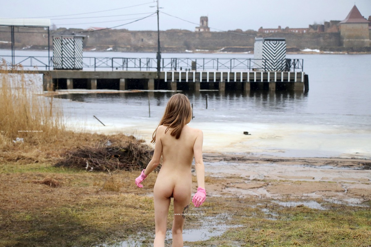Blonde girl Tanja K in pink gloves walks without clothes near an icy lake