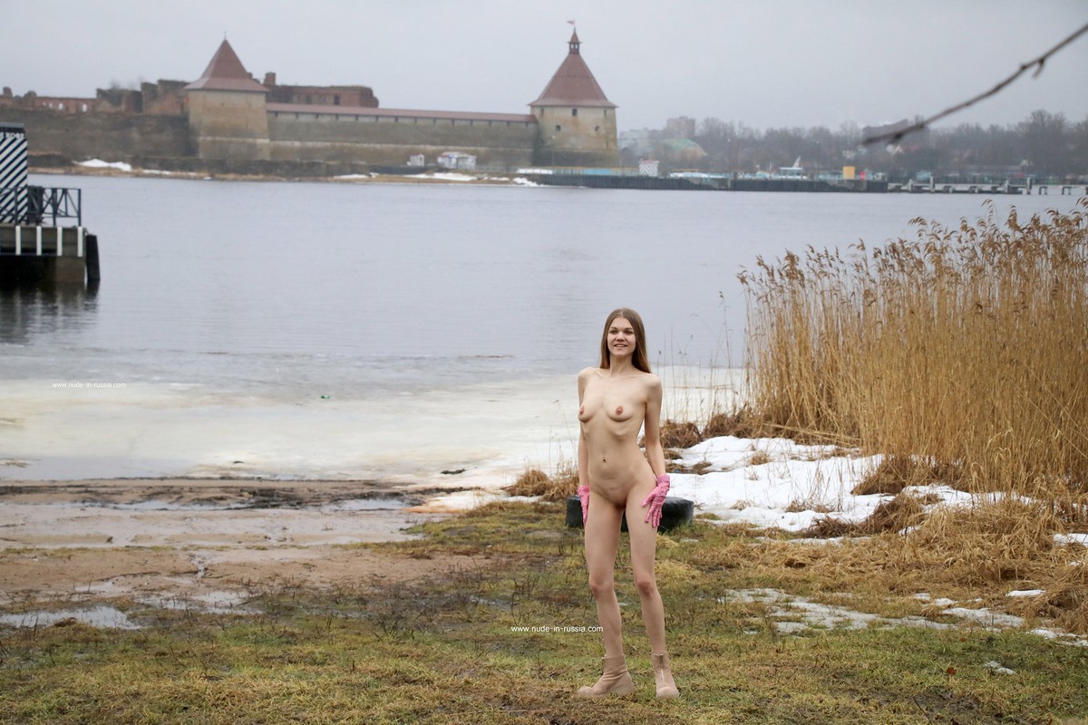 Blonde girl Tanja K in pink gloves walks without clothes near an icy lake