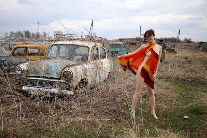 A short-haired naked girl Atisha walks through the museum of old Soviet cars